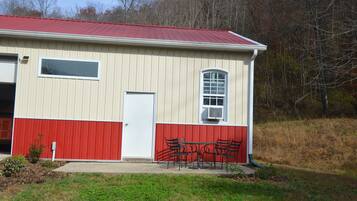 A single-story building with a red and white exterior, a door, a window, and a small outdoor seating area with metal chairs.