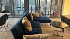 Een moderne woonkamer met een donkerblauwe hoekbank, een klein rond tafeltje en een balkon met rode stoelen.