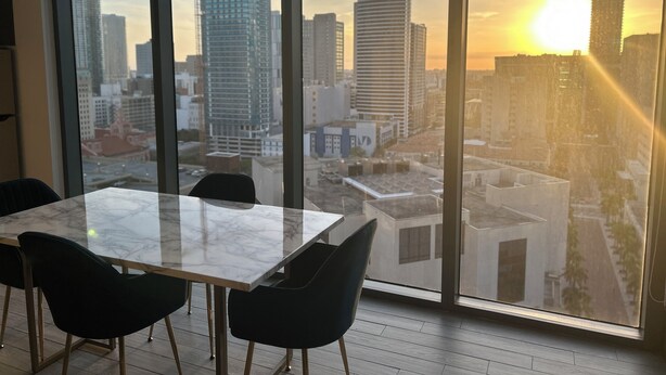 Een moderne eetruimte met een groot raam met uitzicht op een stadsbeeld bij zonsondergang.