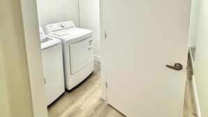 Una lavanderia con lavatrice e asciugatrice, pavimento in legno e una porta bianca.