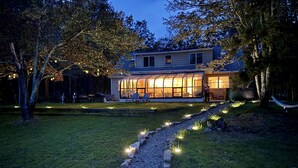A modern house with a glass facade, a well-maintained lawn, and a gravel path with lights. - Lake Views | Tub Sauna Kayak Bike Fire Pit EV (Albrightsville)