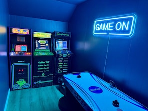 Une salle avec des bornes d’arcade, une table de billard et un panneau néon indiquant « GAME ON ».