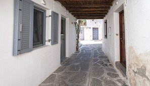 Un carreró estret empedrat, amb parets blanques i persianes, que condueix a una porta blava.