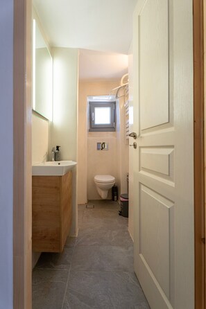 Ein schmales Badezimmer mit einem hölzernen Waschtisch, einer Toilette und einem kleinen Fenster darüber.