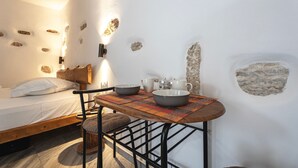 Ein gemütliches Schlafzimmer mit einem hölzernen Bett, einem kleinen Tisch mit Schalen und einem Wasserkocher, sowie einer Wand mit eingemauerten Steinen.