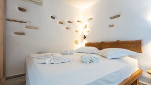 A neatly made bed with white linens and towels, a wooden headboard, and a wall with embedded stones. - El. Passo Cycladic Alley Studio • Paros by ΜΡS (Paros)