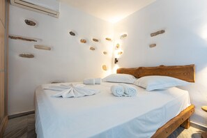 Un llit ben fet amb roba de llit i tovalloles blancs, un panell de fusta al capçal i una paret amb pedres integrades.