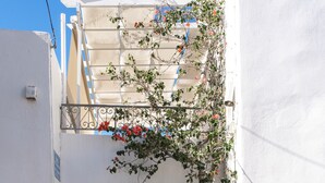Ein schmaler, mit Kopfsteinpflaster belegter Gang mit einer Treppe rechts und einem Balkon mit roten Blumen links.