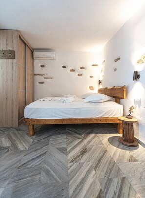 Ein Schlafzimmer mit einem hölzernen Bett, einem kleinen Nachttisch mit Pflanze und einer mit Steinen verzierten Wand.