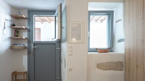 Ein Zimmer mit einer grauen Tür, einem kleinen Holzschemel und einem Fenster mit einem Korb an der Fensterbank.