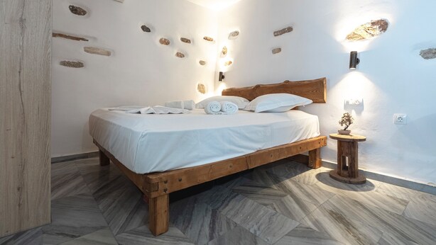 Ein Schlafzimmer mit einem hölzernen Bett, weißen Bettwäsche und einem kleinen Nachttisch mit einer Pflanze.