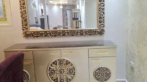 Een kamer met een crèmekleurige kast met decoratieve bloemmotieven, een grote spiegel met een sierlijk frame en een paarse stoel.