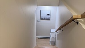 Eine Holztreppe mit Handlauf, die zu einer Zwischenebene mit einem Bilderrahmen und einem Lichtschalter führt.