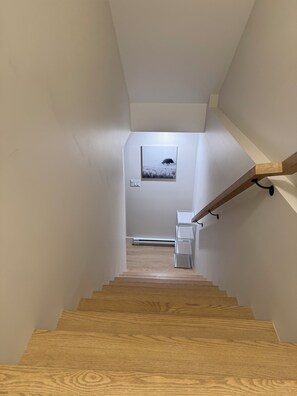 A wooden staircase with a handrail, leading to a landing with a picture frame and a light switch.
