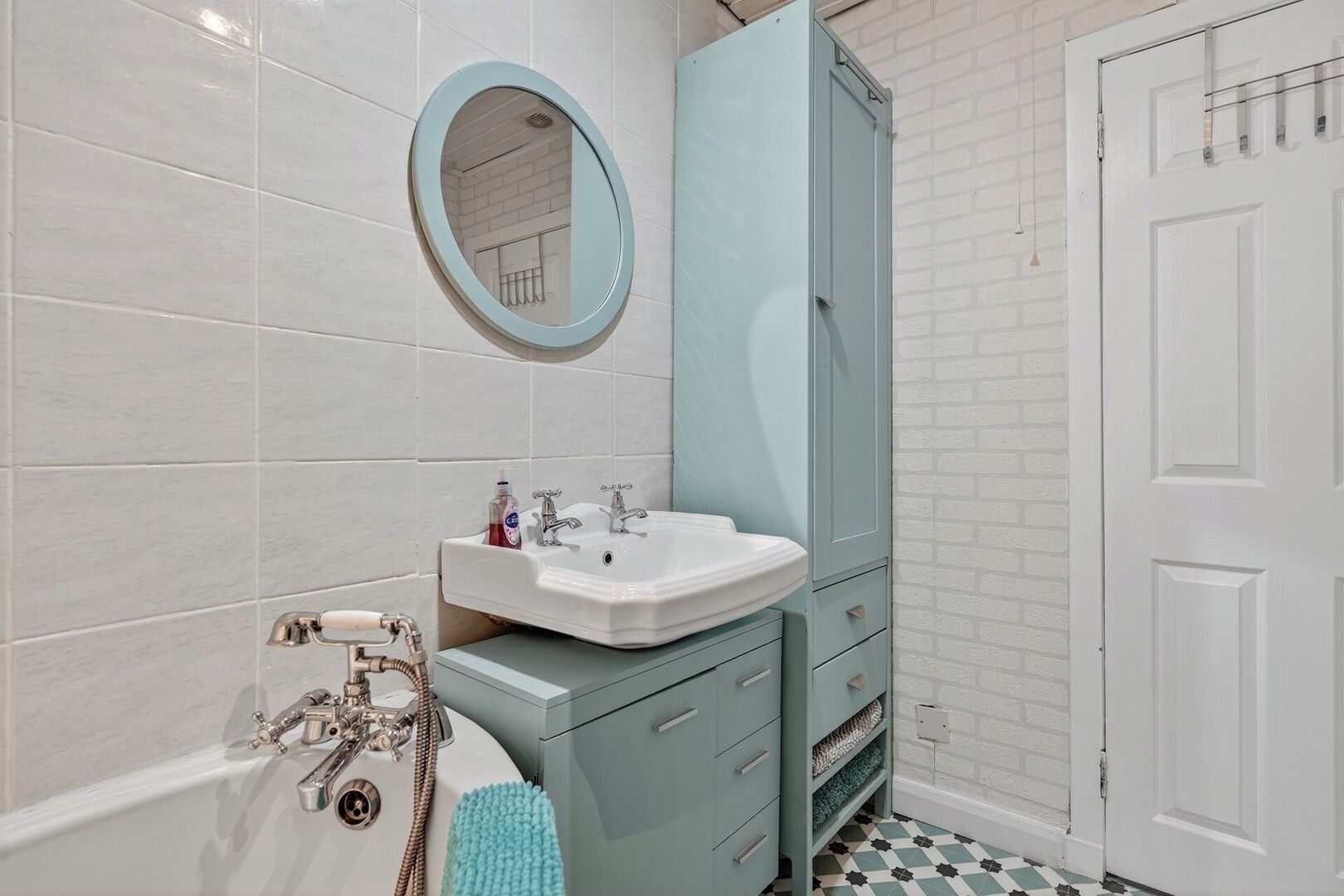 A bathroom with a white bathtub, a white sink with a mirror above it, and a blue cabinet.