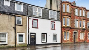 A row of terraced houses with a white facade, black door, and red window frames. - Coastal Charm: Modern Retreat by Seafront (Largs)