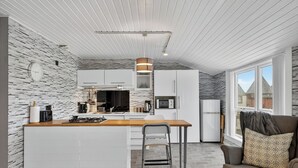 A modern kitchen with a central island, white cabinetry, and a stone-patterned wall. - Coastal Charm: Modern Retreat by Seafront (Largs)
