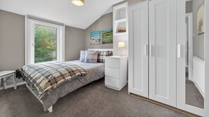 A bedroom with a bed, bedside tables, a wardrobe, and a window. - Coastal Charm: Modern Retreat by Seafront (Largs)