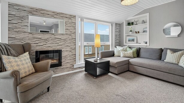 A modern living room with a stone wall, a fireplace, a sofa, and a side table with a lamp. - Coastal Charm: Modern Retreat by Seafront (Largs)