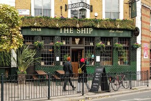 A pub named "The Ship" with a green facade, outdoor seating, and a sign indicating it's a Free House. - Central London Gem: Modern 1BD with Balcony (London)