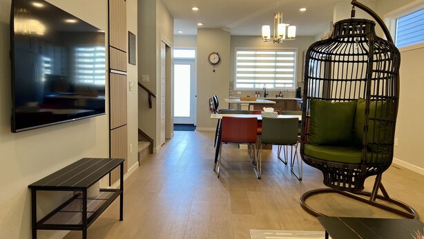 A modern living room with a flat-screen TV, a black metal bench, a green cushioned chair, and a unique black and white patterned chair. - Modern 3BR | Bonus Room | Office | A/C, Smart TVs, Parking (Calgary)