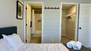 A hotel room with a bed, a bathroom visible through an open door, and a coat rack with hangers. - Modern 3BR | Bonus Room | Office | A/C, Smart TVs, Parking (Calgary)