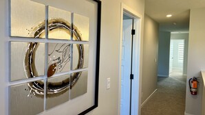 A hallway with a framed abstract art piece on the wall, a white door, and a fire extinguisher mounted on the wall. - Modern 3BR | Bonus Room | Office | A/C, Smart TVs, Parking (Calgary)