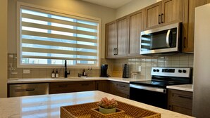A modern kitchen with wooden cabinets, a stainless steel microwave, an oven, and a marble countertop. - Modern 3BR | Bonus Room | Office | A/C, Smart TVs, Parking (Calgary)