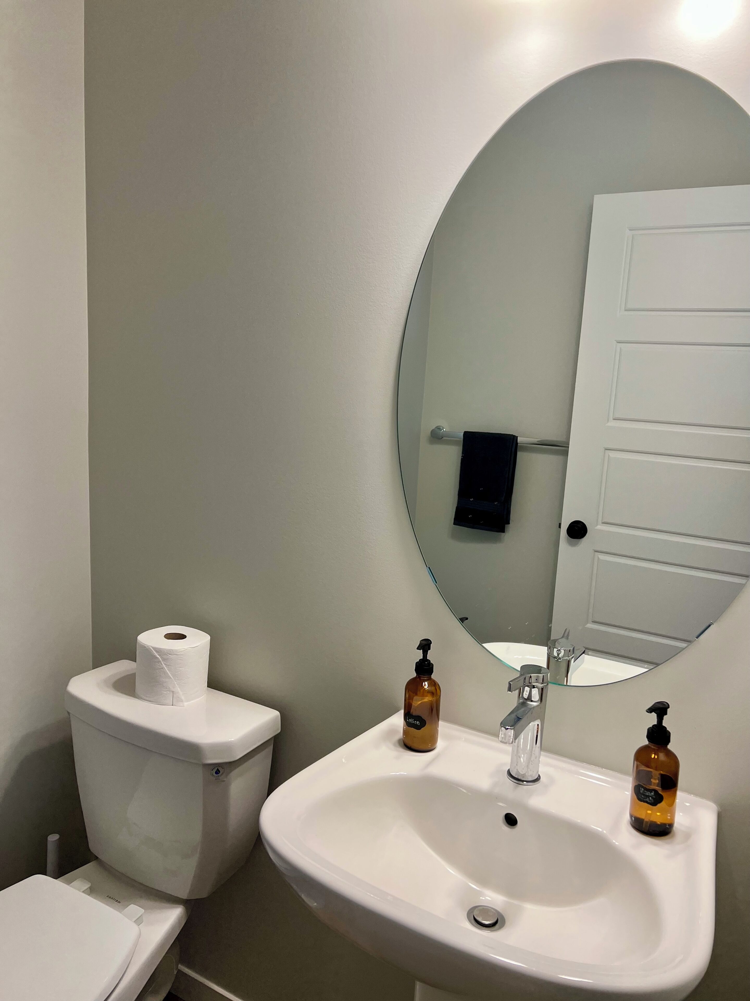Un baño con inodoro, lavamanos con espejo y dos dispensadores de jabón.