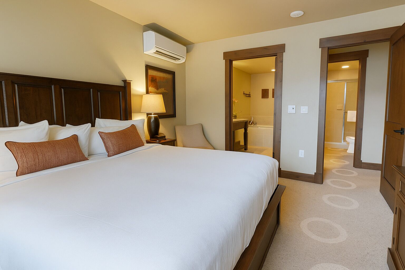 Une chambre d’hôtel avec un grand lit, une table de chevet, une lampe, un appareil de climatisation et une salle de bain visible à travers une porte ouverte.