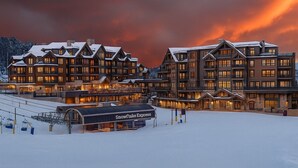 Un grand chalet à plusieurs étages, avec un télésiège en premier plan, le tout entouré de neige.