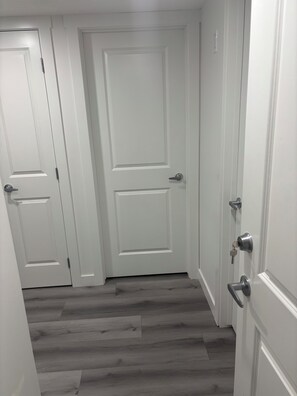 A hallway with white doors and a wooden floor. - Peniel Place - Your Peaceful Home Away From Home (Airdrie)