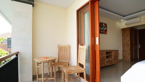 A balcony with a wooden table and chairs, a sliding glass door, and a view of the outside. - Lotus Canggu (Tibubeneng)