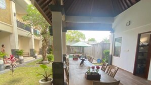 A covered outdoor dining area with a long wooden table and chairs, surrounded by potted plants and a small garden. - Lotus Canggu (Tibubeneng)