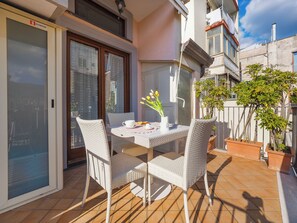 A balcony with a table set for two, two wicker chairs, a potted plant, and a view of the street. - Il Tulipano (Vico Equense)