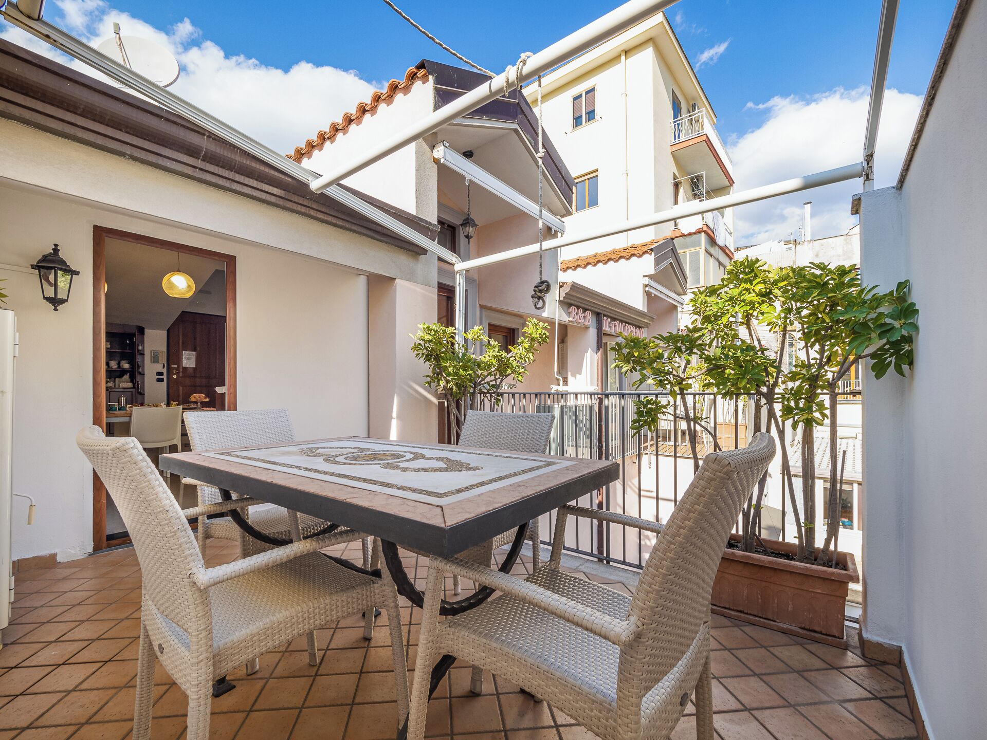 Une terrasse avec une table et des chaises, une plante en pot et un bâtiment en arrière-plan.