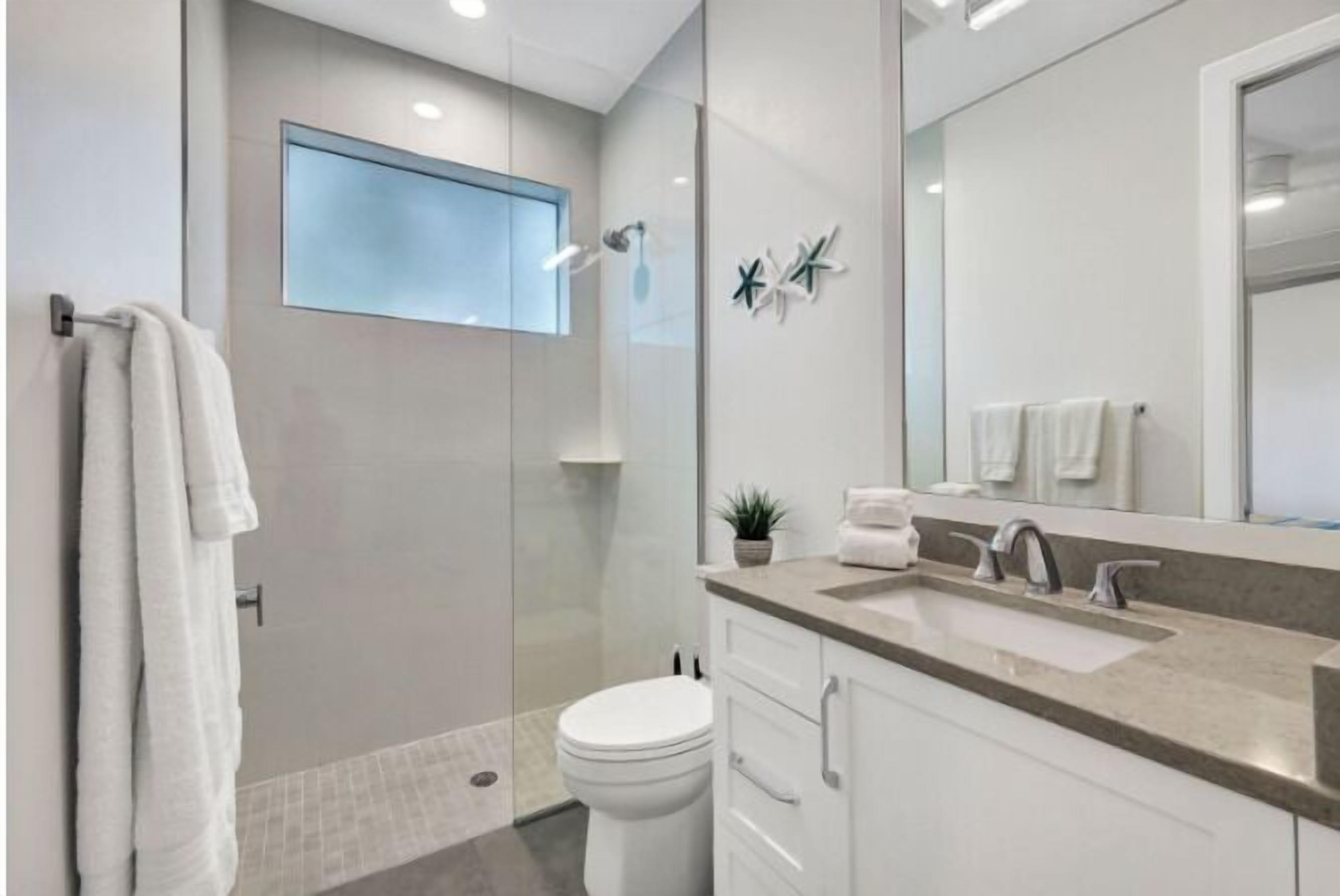 A modern bathroom with a glass-enclosed shower, a large mirror, and a white sink.