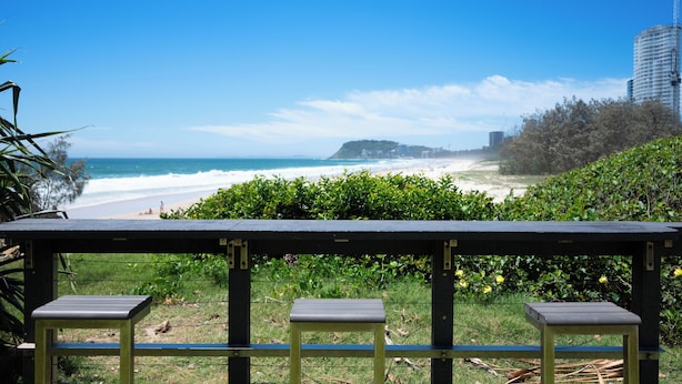 Blick auf einen Strand mit einer Holzterrasse und drei Bänken.