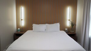 A neatly made bed with white linens, two bedside tables with lamps, and a wooden slat headboard. - Spacious, Sleeps 16+, Game Room Near Downtown Indianapolis (Indianapolis)
