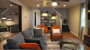 A modern living room with a sofa, chairs, a ceiling fan, and a staircase leading to another level. - Spacious, Sleeps 16+, Game Room Near Downtown Indianapolis (Indianapolis)