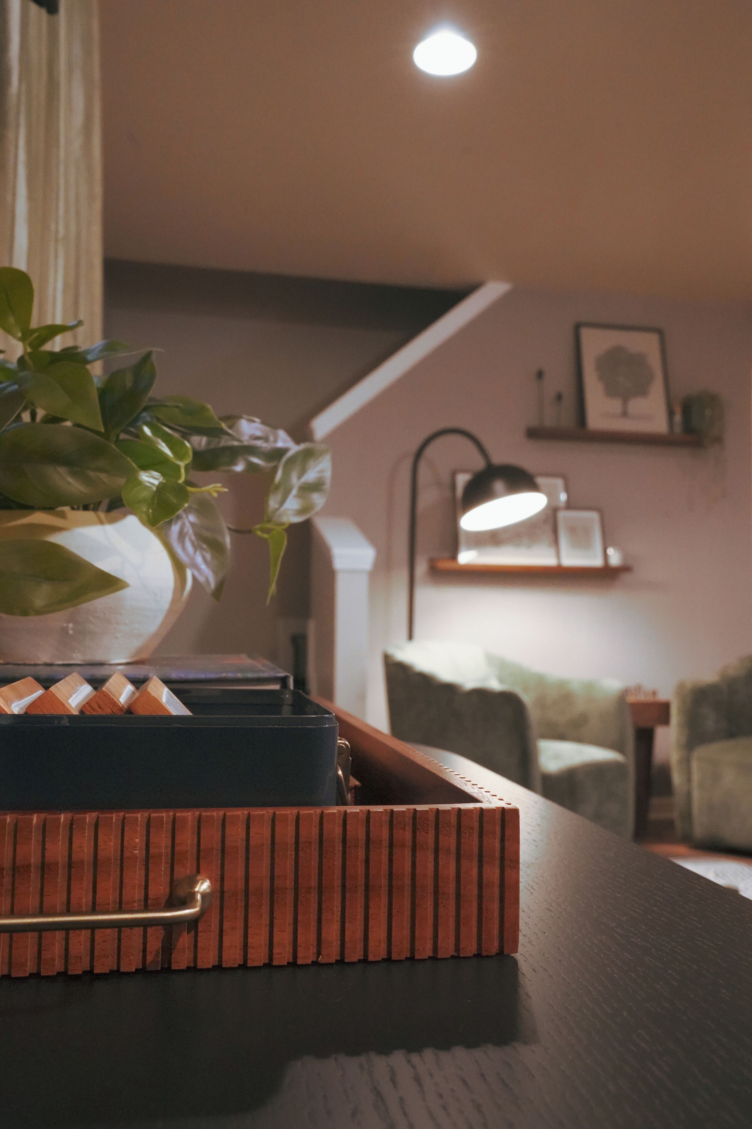 Una bandeja de madera con una planta sobre una mesa, una lámpara y una escalera al fondo.