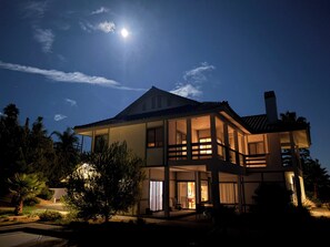 Una casa de dos pisos con balcón, ventanas grandes y un interior visible con un comedor.