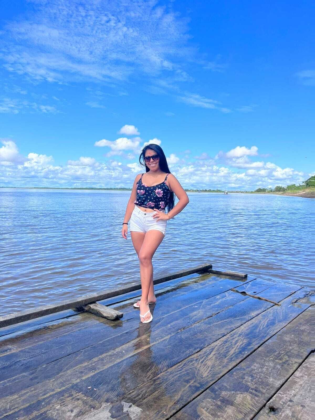 A woman standing on a wooden dock by a calm body of water.