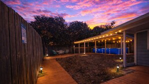 Ein Garten mit Holzzaun, einer überdachten Terrasse mit Lichterketten und einem blauen Pool.