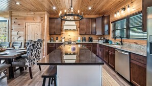 A modern kitchen with wooden paneling, a central island, stainless steel appliances, and a chandelier. - VIEWS! Sleeps 22 | Pool | Theater | Game Rm | (Sevierville)