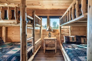 A cabin with wooden walls and a bunk bed with a quilted bedspread. - VIEWS! Sleeps 22 | Pool | Theater | Game Rm | (Sevierville)