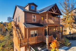 A multi-story wooden cabin with a balcony, a covered porch, and a staircase. - VIEWS! Sleeps 22 | Pool | Theater | Game Rm | (Sevierville)