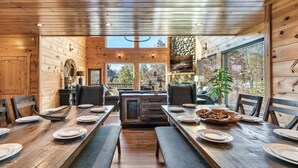 A wooden interior with a long dining table set for four, benches, and a central island with a sink. - VIEWS! Sleeps 22 | Pool | Theater | Game Rm | (Sevierville)
