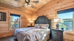 A wooden-paneled bedroom with a bed, nightstands, and a window with a view. - VIEWS! Sleeps 22 | Pool | Theater | Game Rm | (Sevierville)