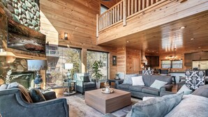 A spacious living area with a high ceiling, wooden walls, and a balcony. There are multiple seating options including sofas and chairs. - VIEWS! Sleeps 22 | Pool | Theater | Game Rm | (Sevierville)